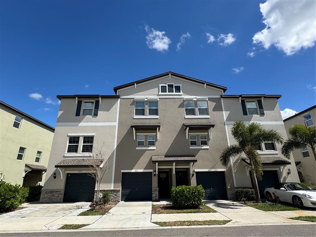 A three-story townhouse exterior with a beige stucco facade and multiple dark-colored garage doors — 840 TENNYSON MILL CIRCLE, TAMPA, FL