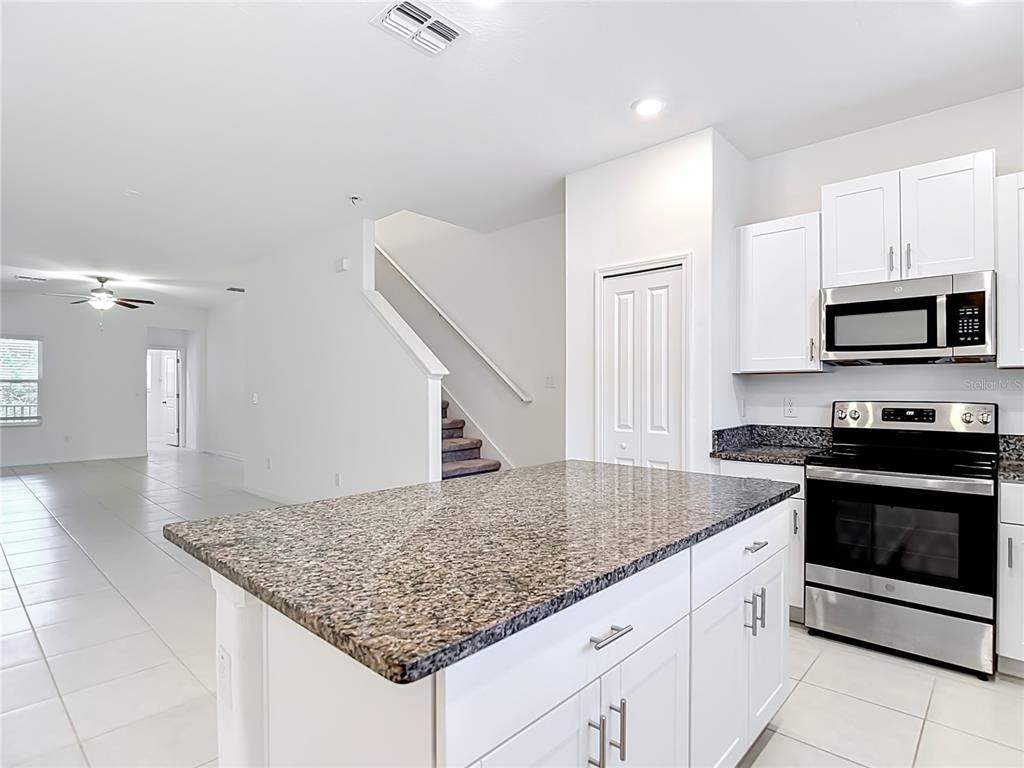 A kitchen with white cabinets, granite countertops, an island, and a view of the stairs — 840 TENNYSON MILL CIRCLE, TAMPA, FL