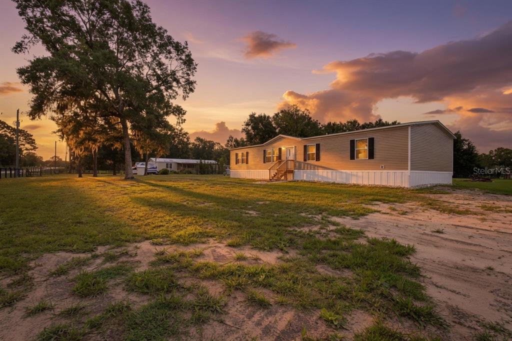 A tan mobile home sits on a grassy lot under a sunset sky — 7250 SW 10TH STREET, OCALA, FL