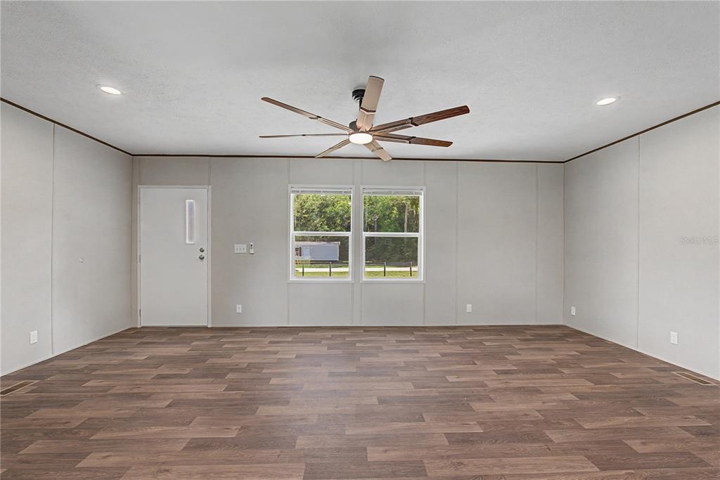 A spacious, empty room features light gray walls, wood-look flooring, a ceiling fan, and windows — 7250 SW 10TH STREET, OCALA, FL
