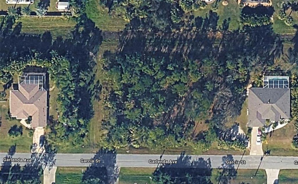 This aerial view shows a vacant, wooded lot situated between two existing residential homes — GARLENDA AVENUE, NORTH PORT, FL