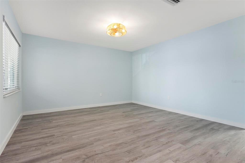 An empty bedroom features light blue walls, wood-look flooring, and a central ceiling light fixture — 1258 BARBARA DRIVE UNIT 107, VENICE, FL