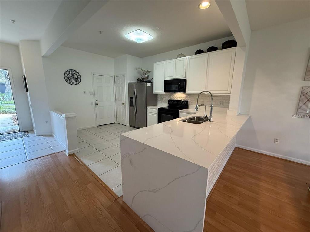 A kitchen features white cabinets, a quartz-topped island, and a mix of tile and wood flooring — 6235 GOETHE STREET UNIT 106, ORLANDO, FL