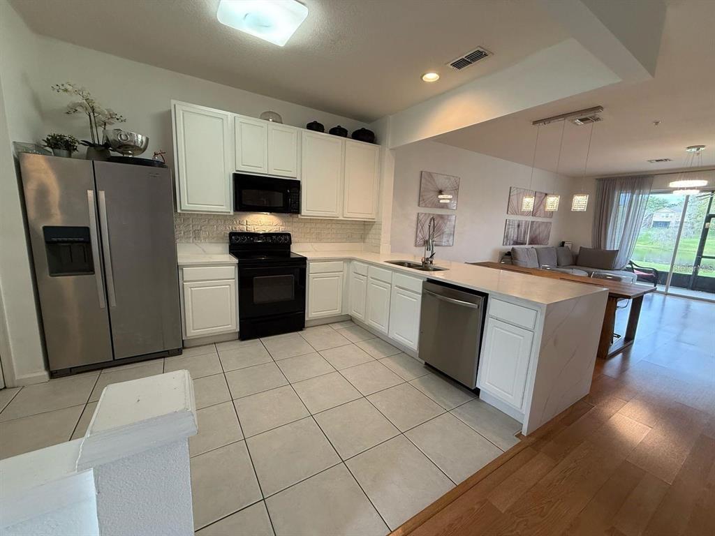 A kitchen with white cabinets, stainless steel appliances, and tile flooring opens to a dining area — 6235 GOETHE STREET UNIT 106, ORLANDO, FL