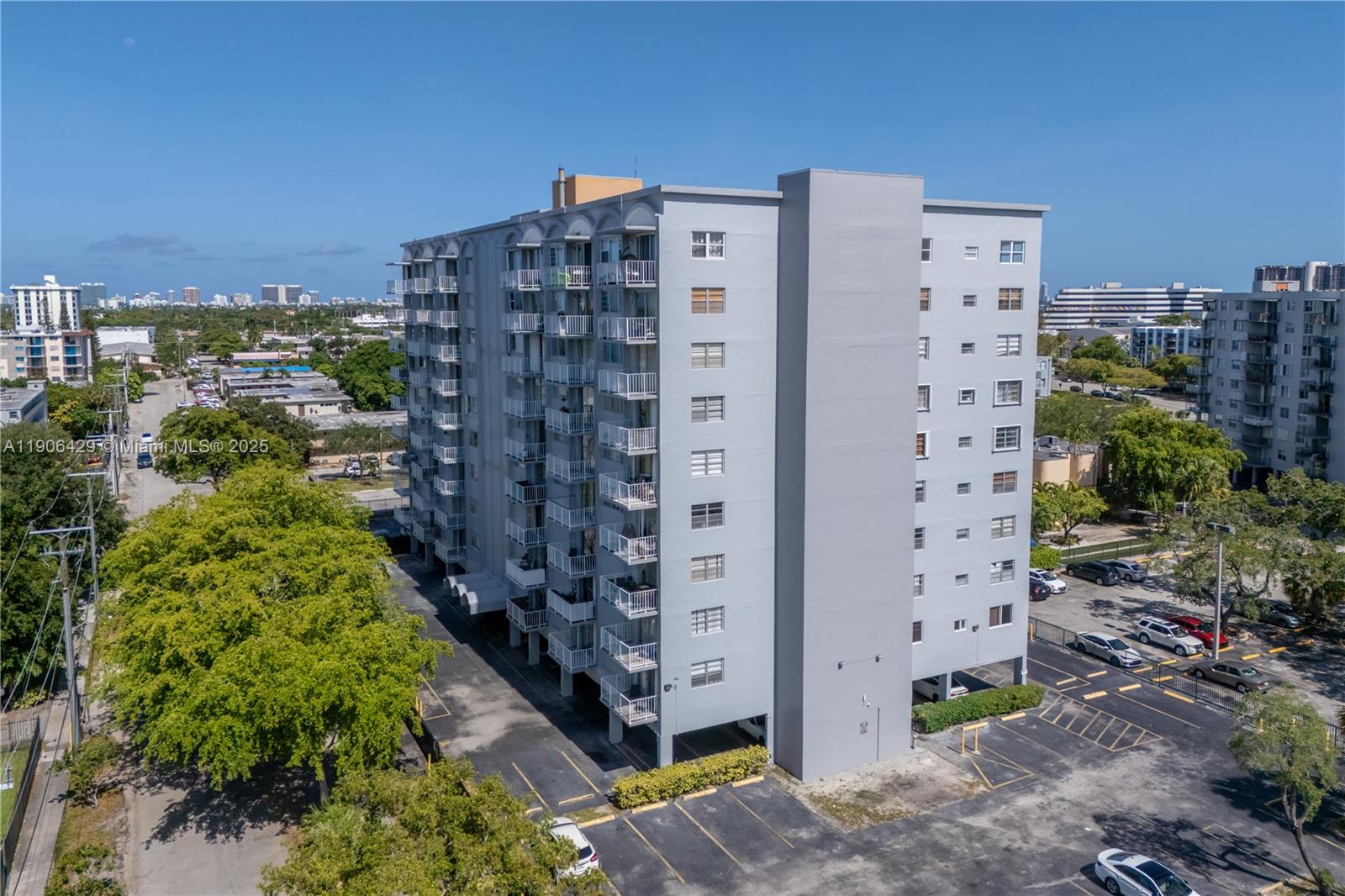 An aerial view shows a multi-story gray apartment building with balconies and a parking lot — 1470 NE 125th Ter, North Miami FL 33161, NORTH MIAMI, FL