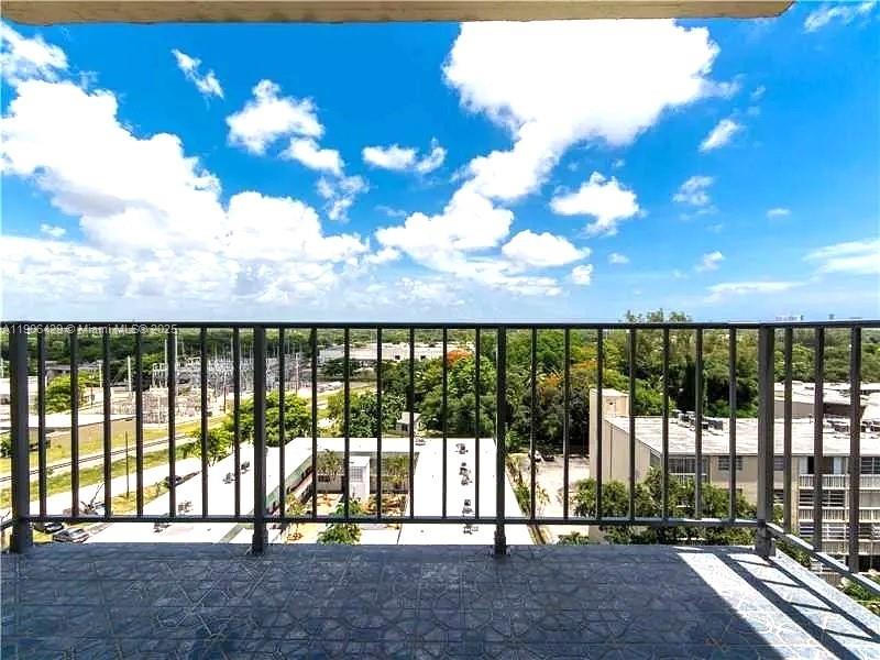 A balcony with a metal railing overlooks a suburban landscape under a cloudy blue sky — 1470 NE 125th Ter, North Miami FL 33161, NORTH MIAMI, FL