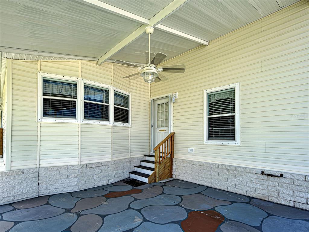 A covered patio with a ceiling fan, stone-patterned flooring, and light-colored vinyl siding — 6562 HIKINA DRIVE, NORTH PORT, FL
