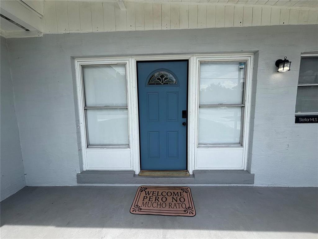 A blue front door with side windows and a welcome mat on a covered porch — 6035 SAGE DRIVE, ORLANDO, FL