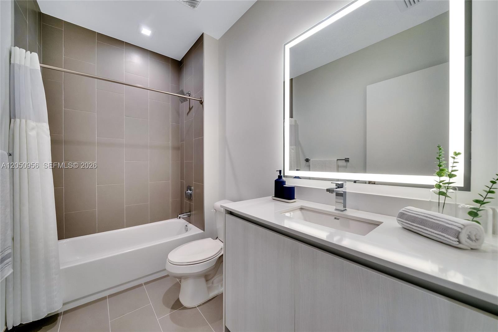 A modern bathroom features a white vanity, a backlit mirror, and a tiled shower-tub combination — 1809 Jackson St, Hollywood FL 33020, HOLLYWOOD, FL