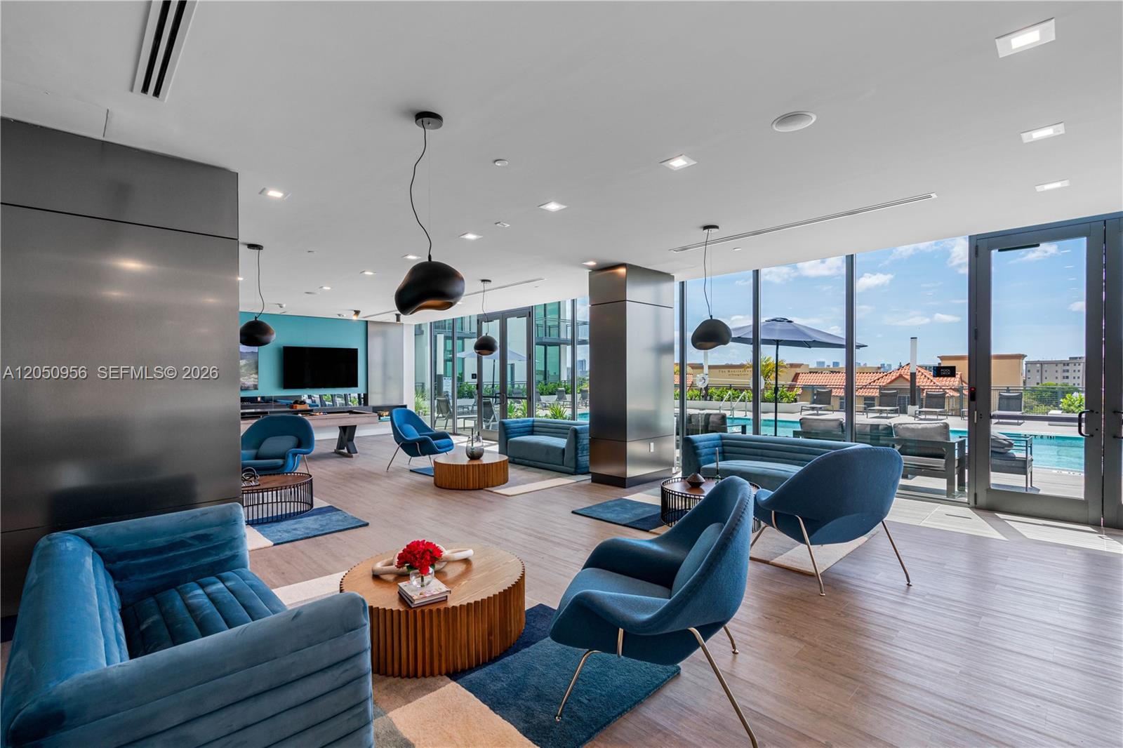 A modern lounge area features blue velvet furniture, wood coffee tables, and floor-to-ceiling windows — 1809 Jackson St, Hollywood FL 33020, HOLLYWOOD, FL