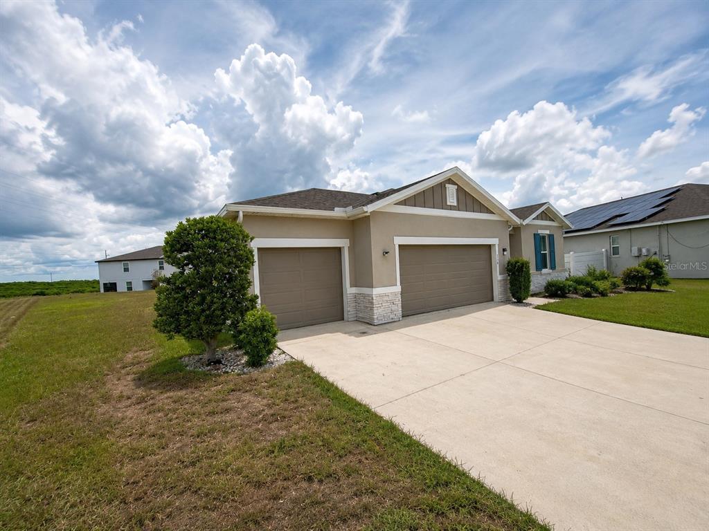 A tan single-story house with a three-car garage and stone accents under a cloudy sky — 236 HILLCREST DRIVE, DUNDEE, FL