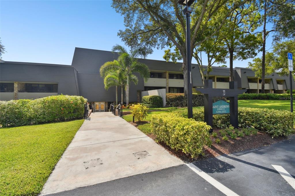 A concrete walkway leads to the entrance of a multi-story building with dark siding — 36750 US HIGHWAY 19 UNIT 23-110, PALM HARBOR, FL