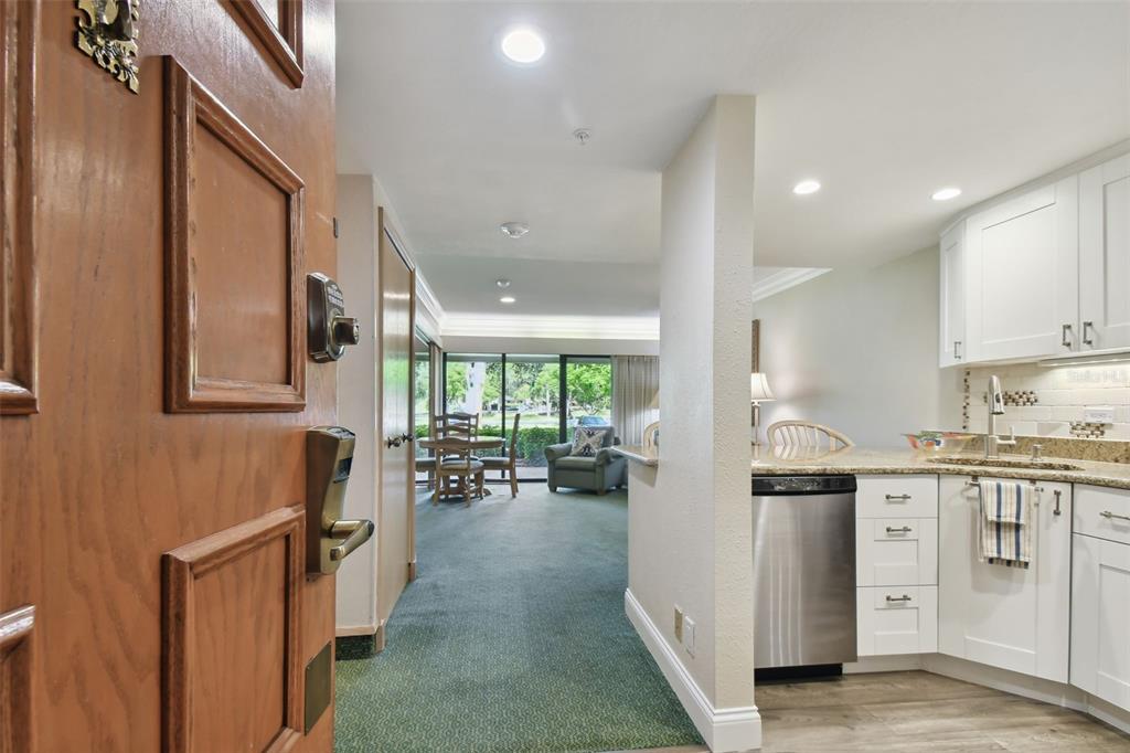A view from an entryway into a kitchen with white cabinets and a carpeted living area — 36750 US HIGHWAY 19 UNIT 23-110, PALM HARBOR, FL