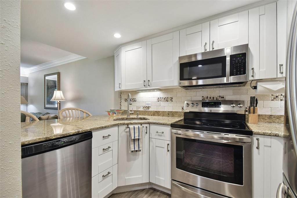 A kitchen features white cabinets, granite countertops, stainless steel appliances, and a subway tile backsplash — 36750 US HIGHWAY 19 UNIT 23-110, PALM HARBOR, FL