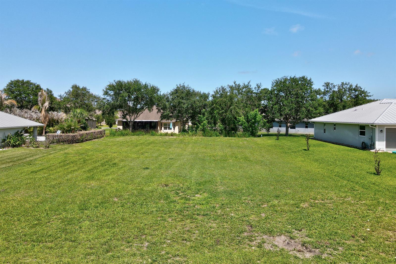 A large, grassy backyard sits between two houses with trees in the background — 6370 Tropical Way, Vero Beach FL 32967, VERO BEACH, FL