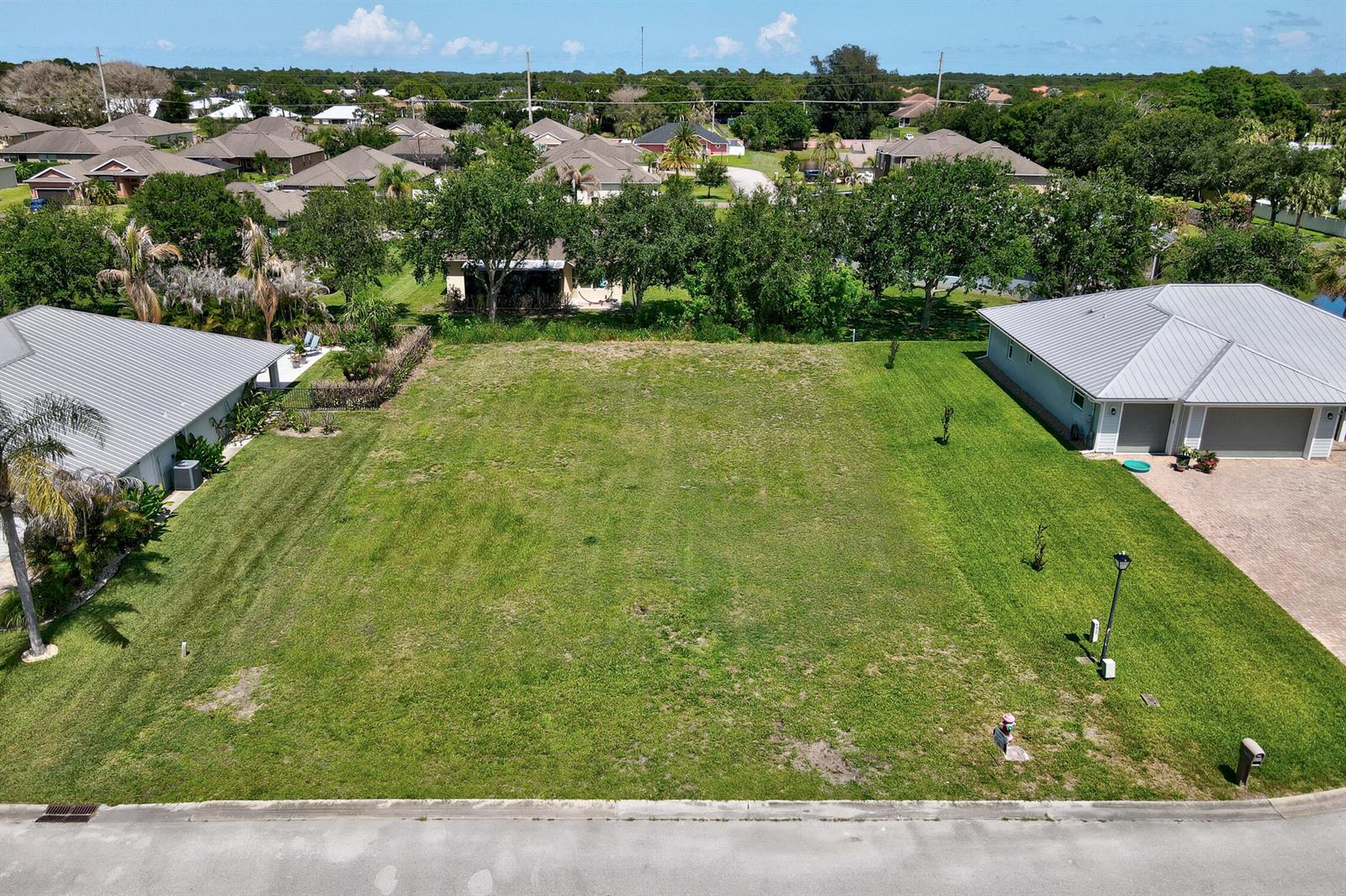 An aerial view shows a vacant residential lot situated between two houses on a street — 6370 Tropical Way, Vero Beach FL 32967, VERO BEACH, FL