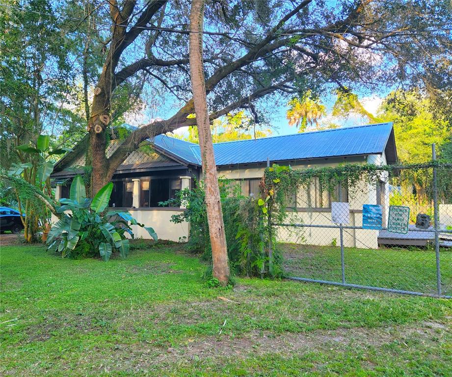 A single-story house with a blue metal roof sits behind a chain-link fence — 7805 N 12TH STREET, TAMPA, FL
