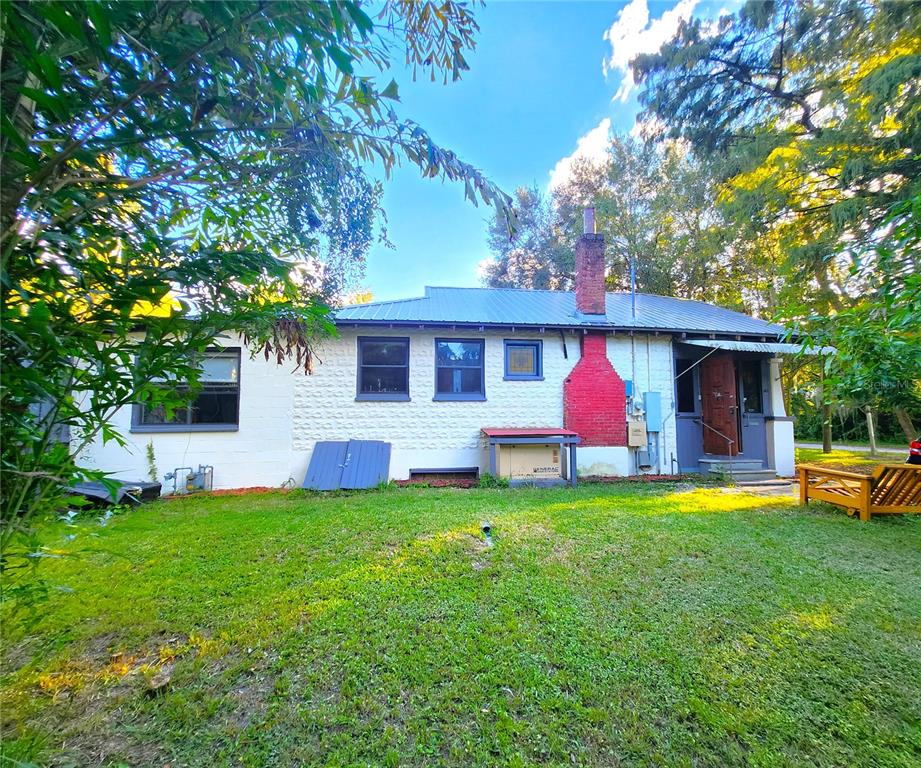 The exterior of a white brick house features a red chimney and a metal roof — 7805 N 12TH STREET, TAMPA, FL