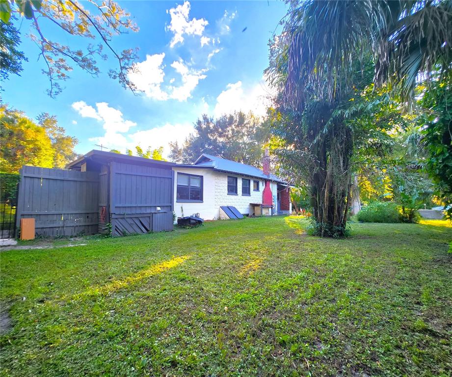 The exterior of a white house features a wooden fence and a large backyard tree — 7805 N 12TH STREET, TAMPA, FL