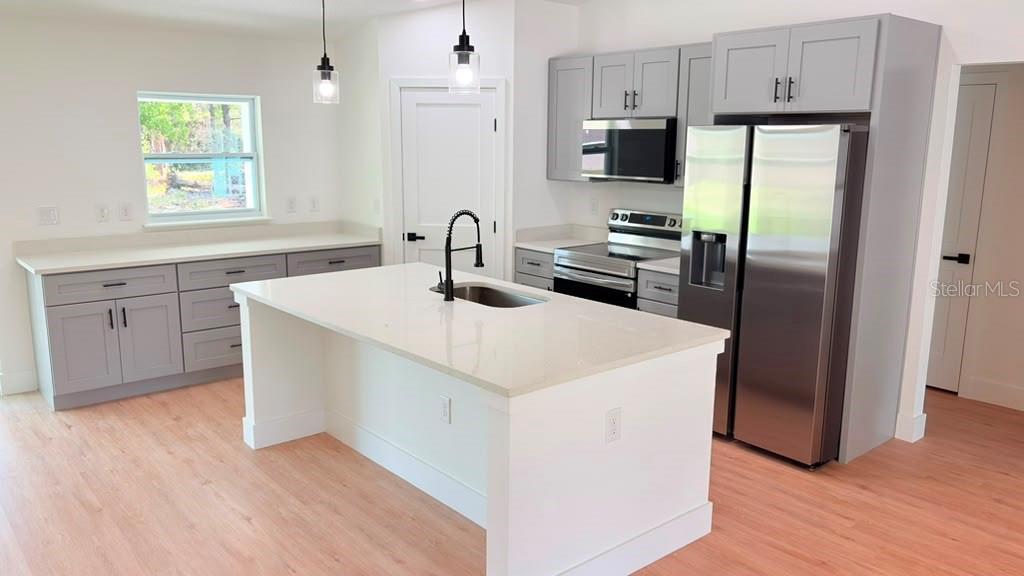 An open-concept kitchen and living area features light wood flooring, white walls, and gray cabinetry — 17 MALAUKA RUN DRIVE, OCKLAWAHA, FL