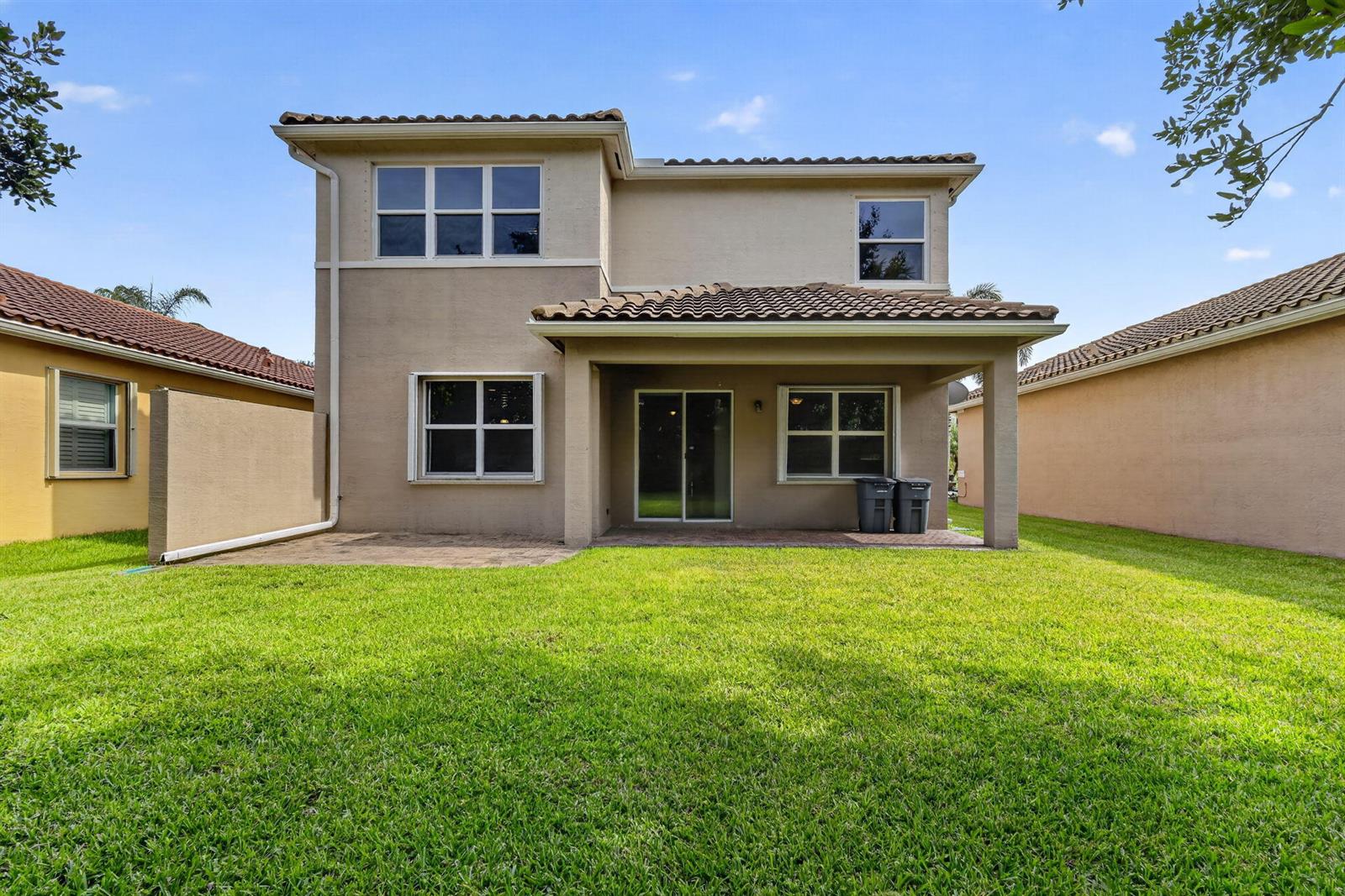The exterior rear view of a two-story beige stucco house with a covered patio — 8135 Cantabria Falls Drive, Boynton Beach FL 33473, BOYNTON BEACH, FL