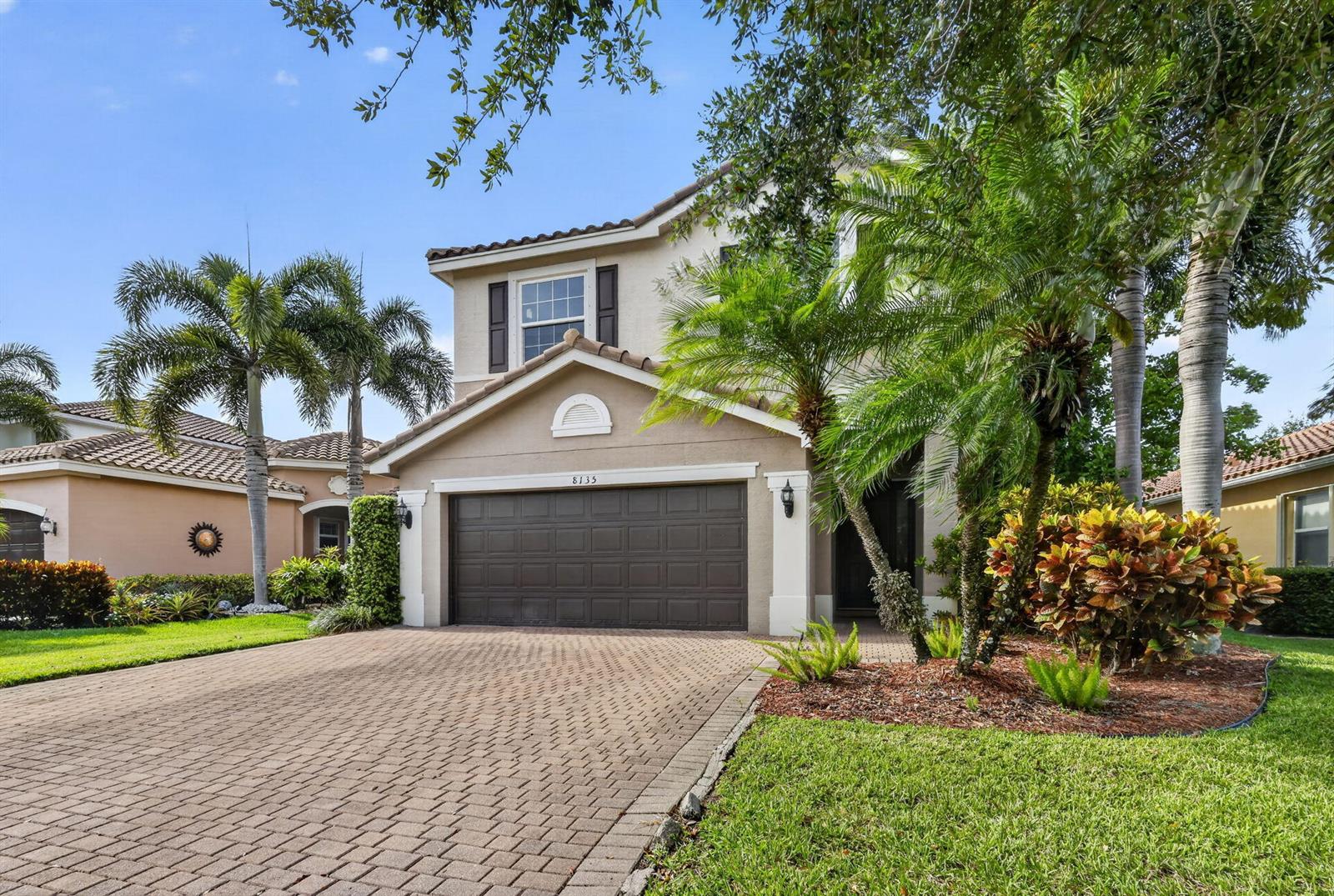 A two-story suburban house features a paved driveway, a garage, and tropical landscaping — 8135 Cantabria Falls Drive, Boynton Beach FL 33473, BOYNTON BEACH, FL