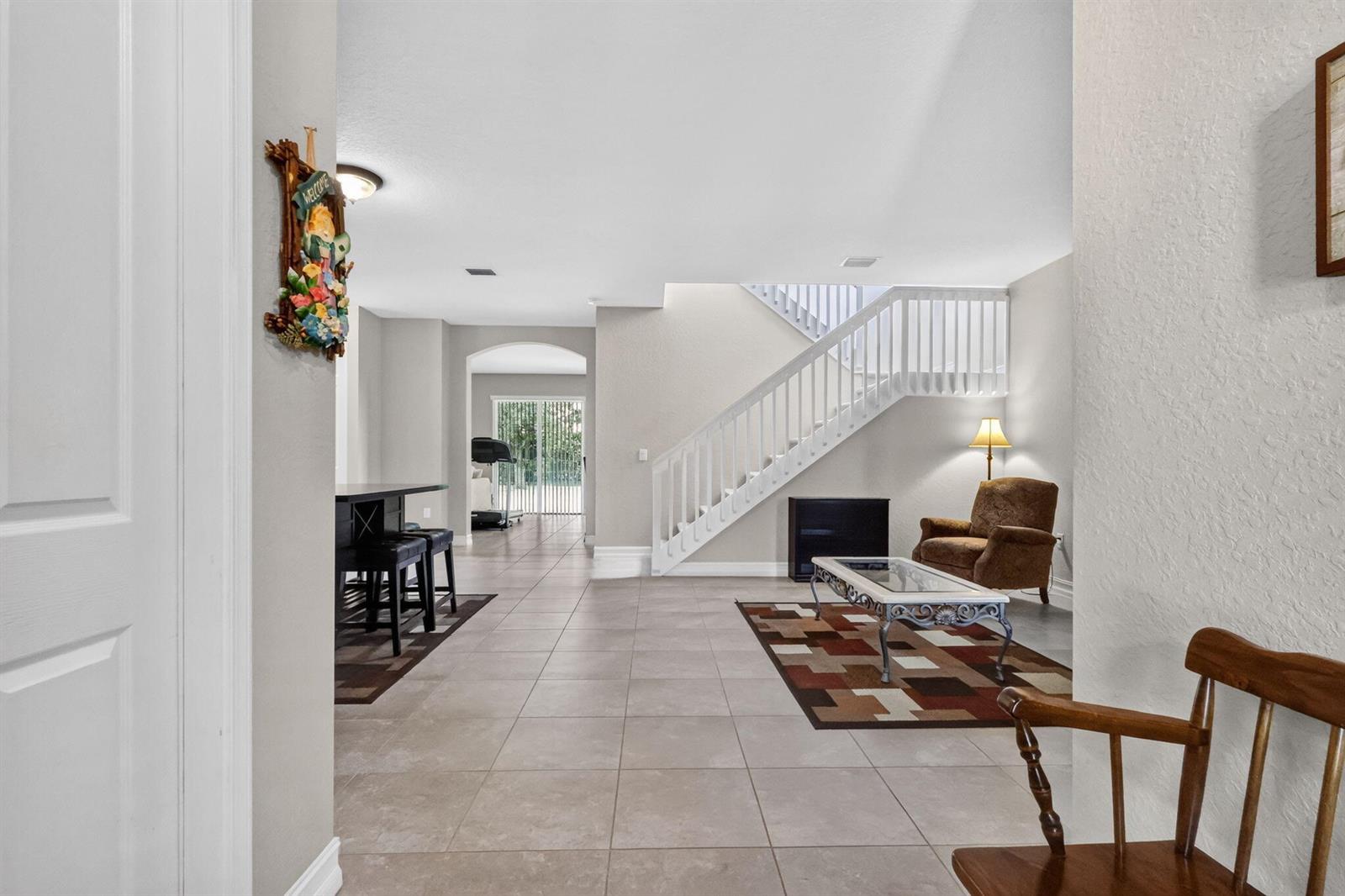 An open-concept living area features tile flooring, a white staircase, and a dining space — 8135 Cantabria Falls Drive, Boynton Beach FL 33473, BOYNTON BEACH, FL