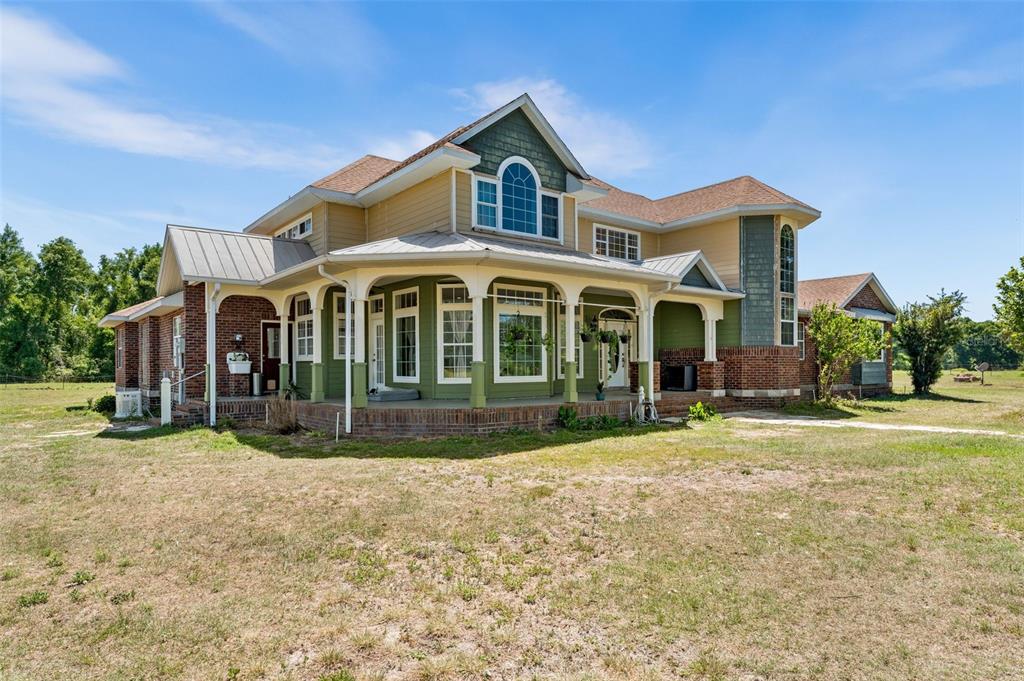 A two-story house with brick and siding exterior features a wraparound porch and metal roof — 20952 60TH TERRACE, LIVE OAK, FL