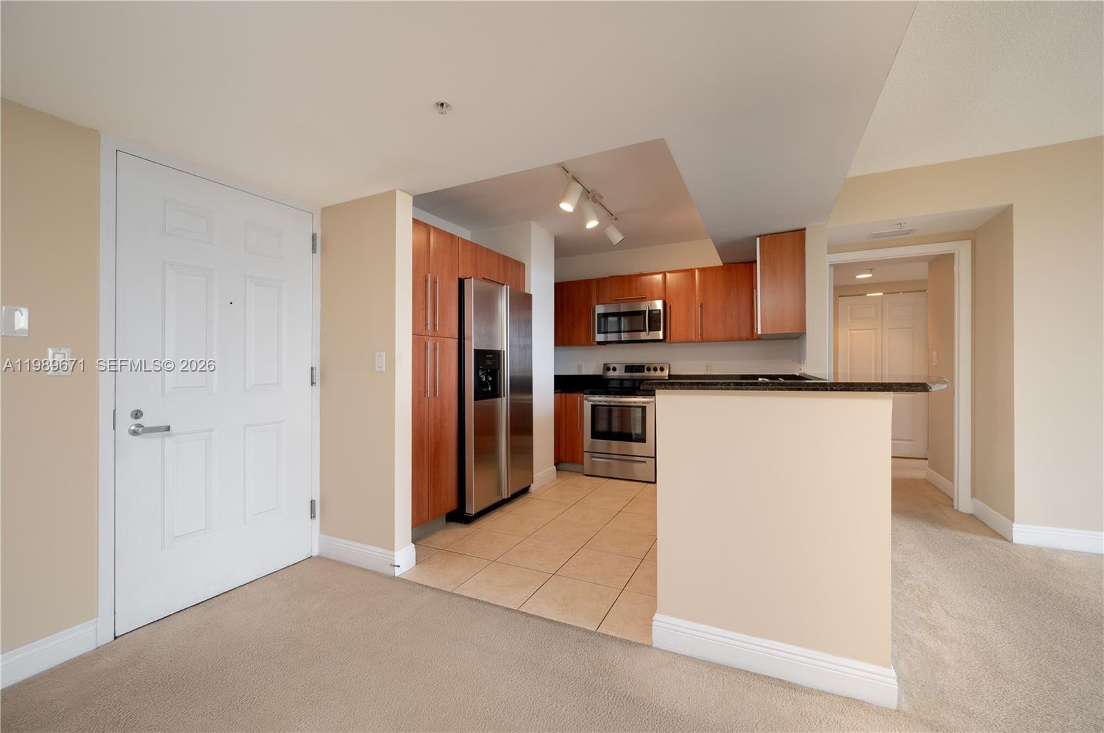 A kitchen with wood cabinets, stainless steel appliances, and tile flooring sits beside an entryway — 3232 SW Coral Way # 1504, Miami FL 33145, MIAMI, FL