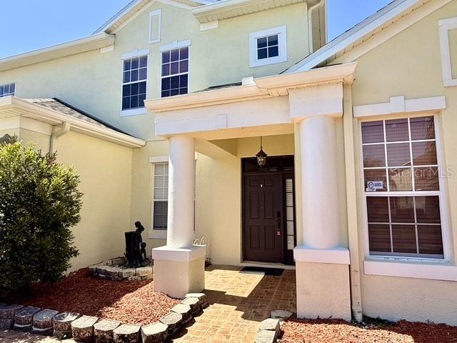 The exterior of a two-story house features a covered entryway with columns and tan siding — 2300 THE OAKS BOULEVARD, KISSIMMEE, FL