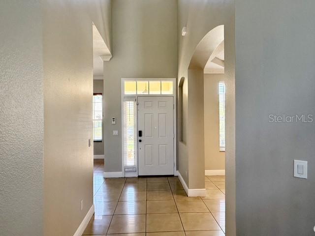 An entryway with a white front door, high ceilings, and light-colored tile flooring — 2300 THE OAKS BOULEVARD, KISSIMMEE, FL
