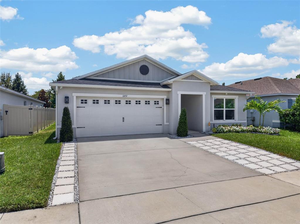 A single-story house with a two-car garage, light gray exterior, and a concrete driveway — 13737 RUSHING CREEK RUN, ORLANDO, FL