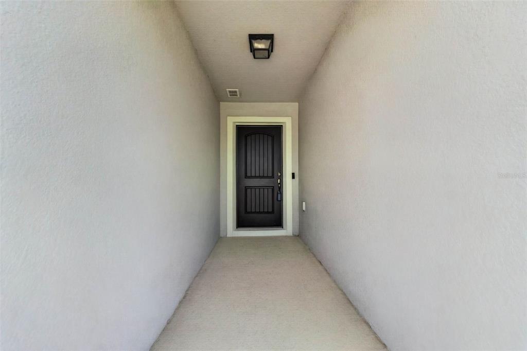 A covered entryway features a dark front door flanked by plain, light-colored stucco walls — 13737 RUSHING CREEK RUN, ORLANDO, FL