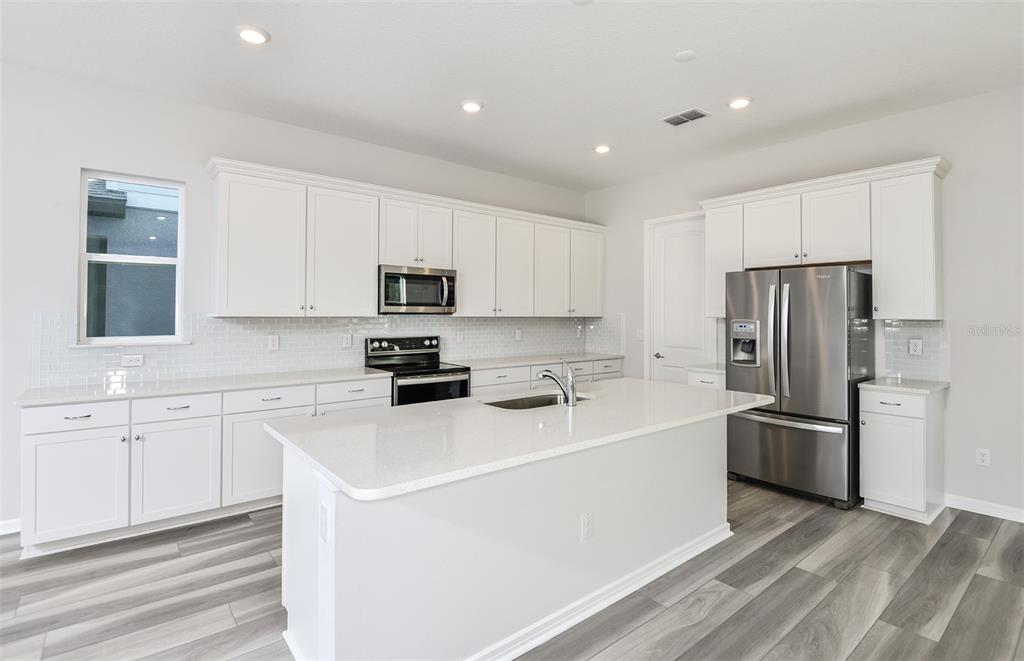 A modern kitchen features white cabinetry, stainless steel appliances, a center island, and wood-look flooring — 1384 ALLAGASH DRIVE, ZEPHYRHILLS, FL