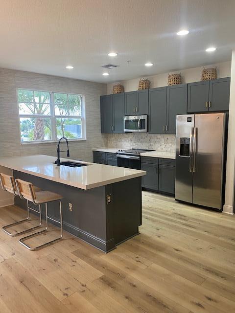 A kitchen features dark gray cabinets, a quartz-topped island with stools, and light wood flooring — 229 N Latitude Circle, Delray Beach FL 33483, DELRAY BEACH, FL