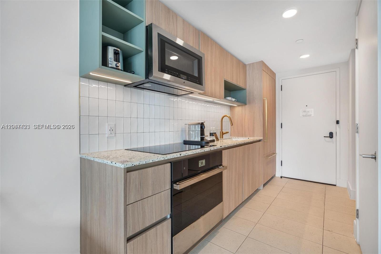 A modern kitchen features light wood cabinets, a speckled countertop, and a white tiled backsplash — 159 NE 6th St # 3212, Miami FL 33132, MIAMI, FL