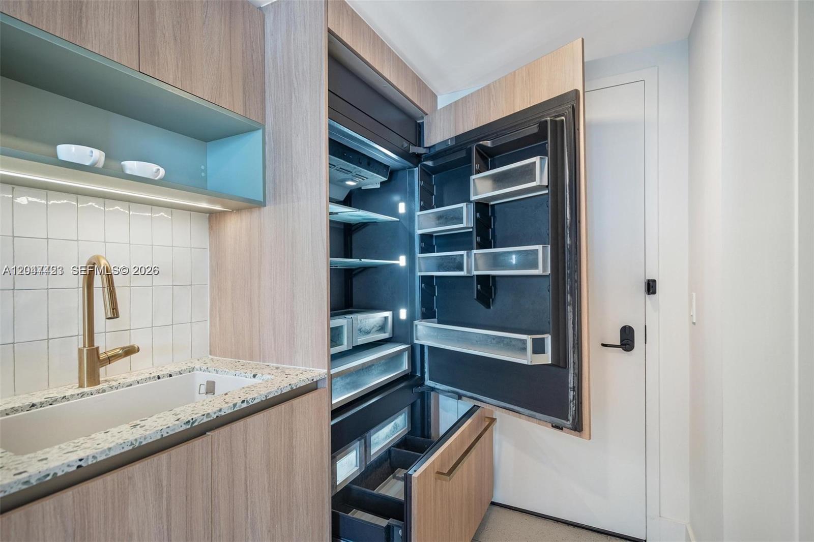 A modern kitchen features light wood cabinetry, a gold faucet, and an integrated refrigerator — 159 NE 6th St # 3212, Miami FL 33132, MIAMI, FL