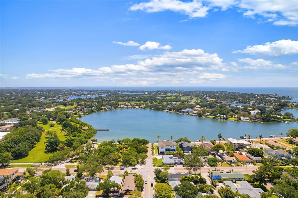 An aerial view shows a lake surrounded by residential homes, trees, and a blue sky — 144 30TH AVENUE NE, ST PETERSBURG, FL