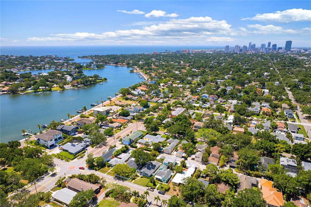 An aerial view shows a coastal residential neighborhood with a waterway and a distant city skyline — 144 30TH AVENUE NE, ST PETERSBURG, FL