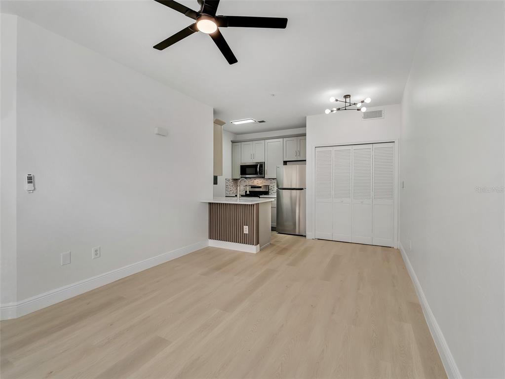 This open-concept living area features light wood flooring, a kitchen island, and a ceiling fan — 8933 LEE VISTA BOULEVARD UNIT 2607, ORLANDO, FL