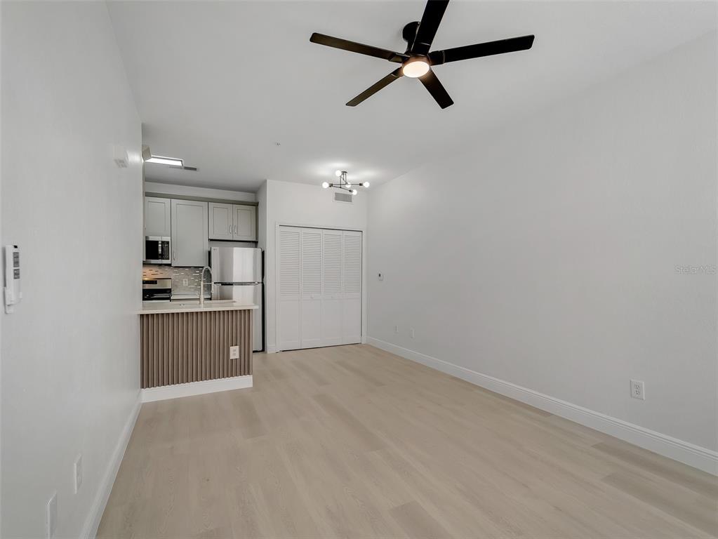 A bright, open-concept living area features light wood flooring, a ceiling fan, and a kitchen — 8933 LEE VISTA BOULEVARD UNIT 2607, ORLANDO, FL
