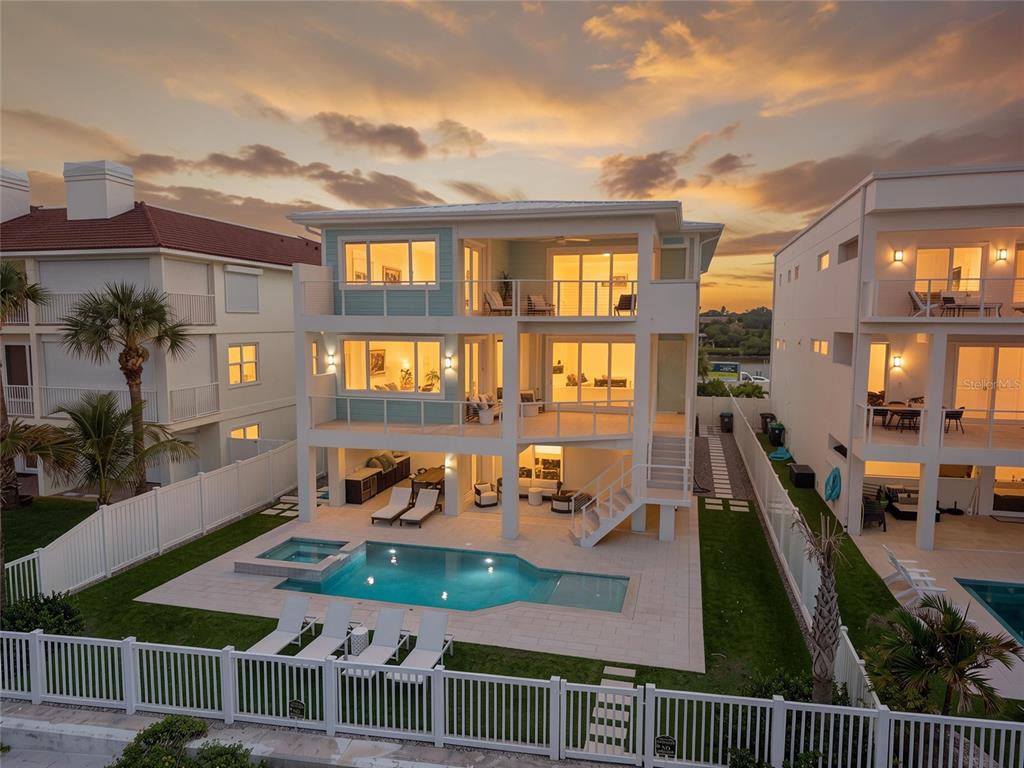 A three-story coastal home features a swimming pool, balconies, and a white fence at sunset — 34 GULF BOULEVARD, INDIAN ROCKS BEACH, FL