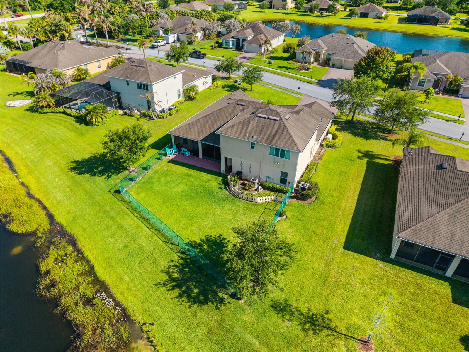 An aerial view of a two-story suburban house with a fenced backyard and a pond — VERO BEACH, FL