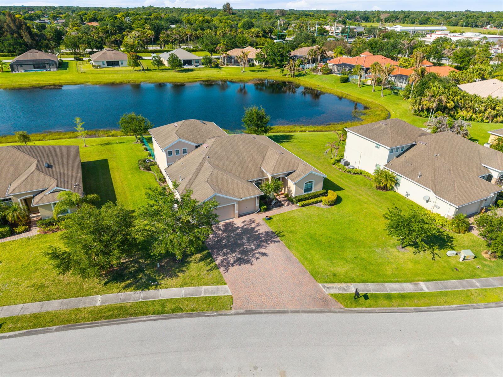 An aerial view shows a suburban house with a paved driveway and a backyard pond — VERO BEACH, FL
