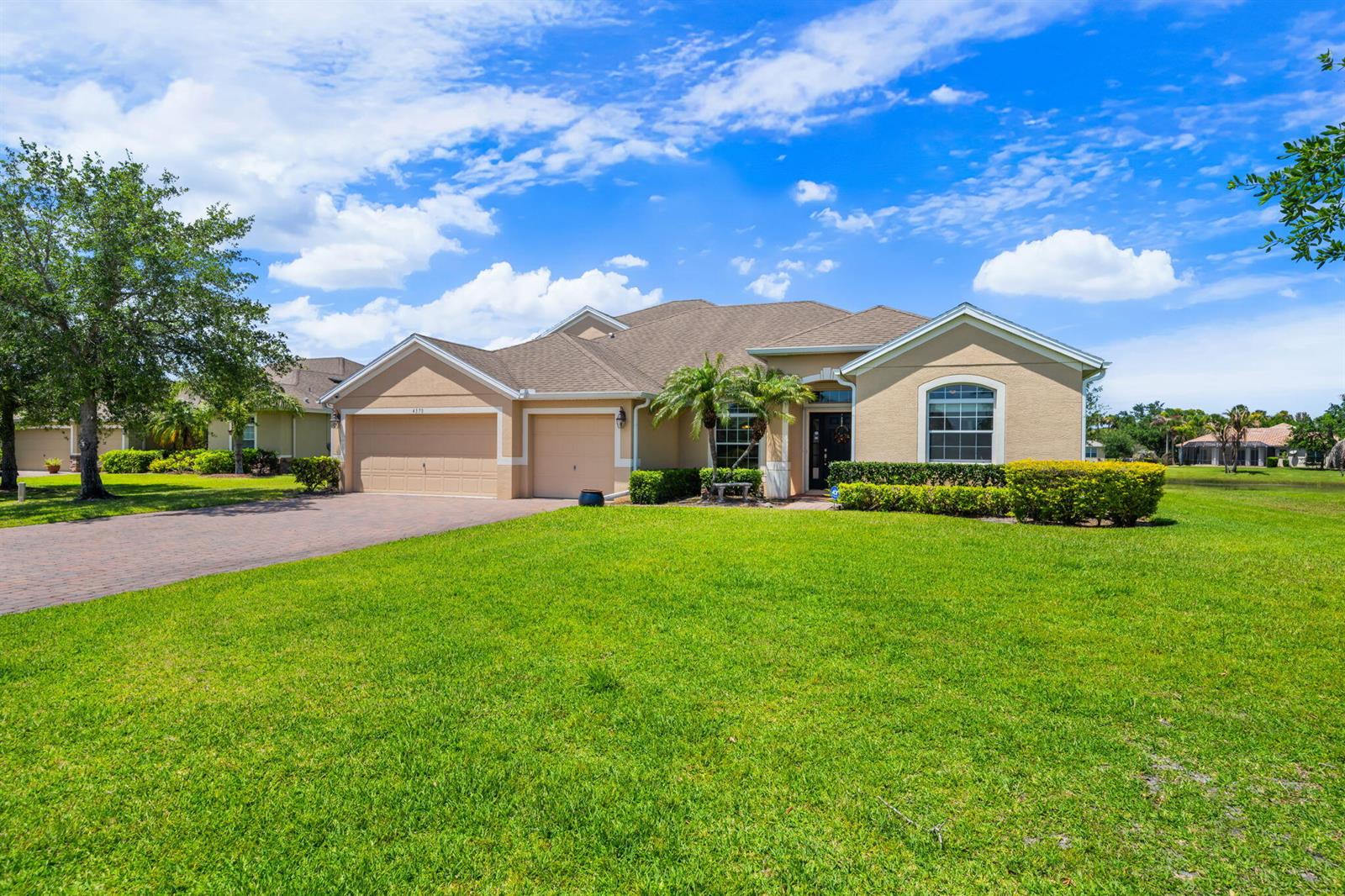 A tan single-story house with a brick driveway, two-car garage, and a large front lawn — VERO BEACH, FL