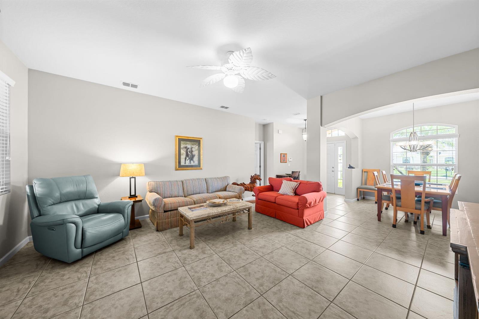 This virtually staged living and dining area features neutral furniture, tile flooring, and a ceiling fan — VERO BEACH, FL