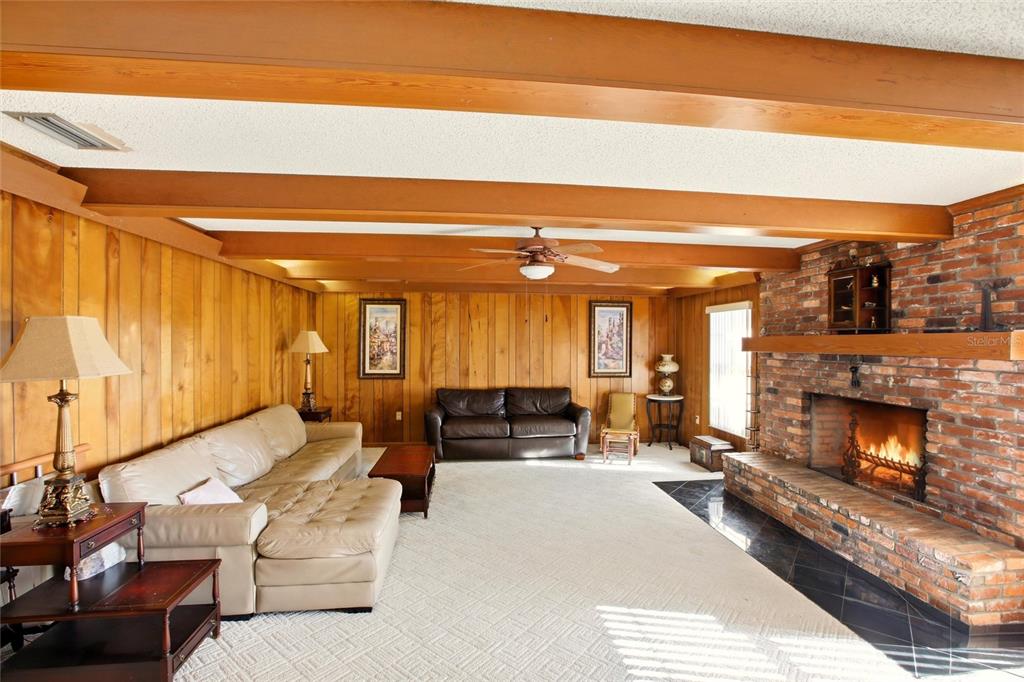 A living room features wood-paneled walls, exposed ceiling beams, a brick fireplace, and carpeted flooring — 3903 EDISON AVENUE, BOWLING GREEN, FL