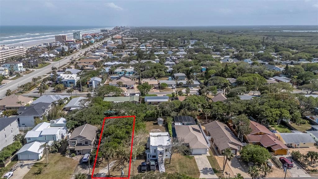 An aerial view shows a vacant, rectangular lot outlined in red between two residential houses — E 12TH AVENUE, NEW SMYRNA BEACH, FL