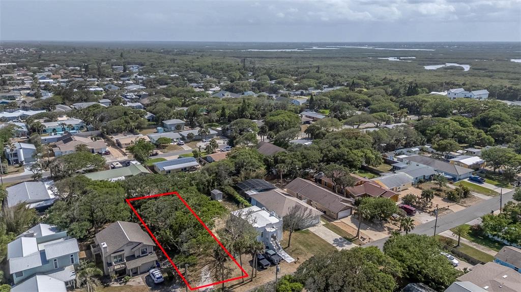 An aerial view shows a vacant, tree-covered lot outlined in red between two residential houses — E 12TH AVENUE, NEW SMYRNA BEACH, FL