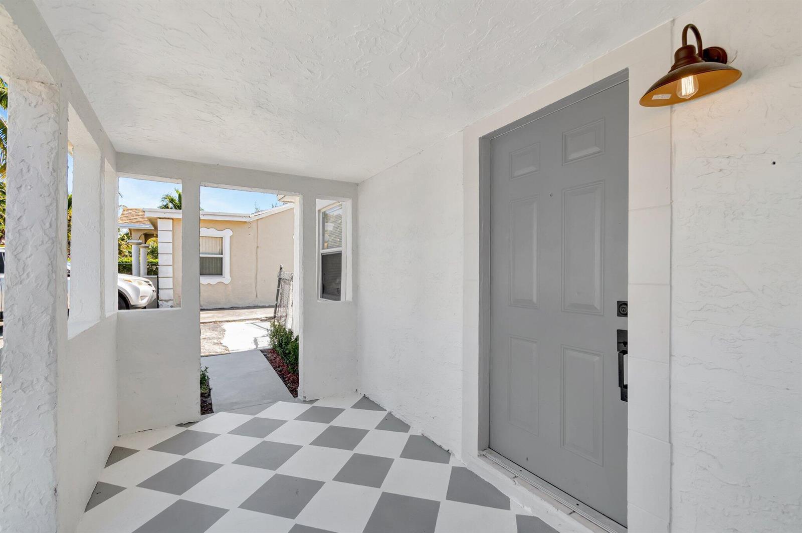A covered entryway features a gray door, a checkered floor, and a wall-mounted light fixture — 950 29th Street, West Palm Beach FL 33407, WEST PALM BEACH, FL